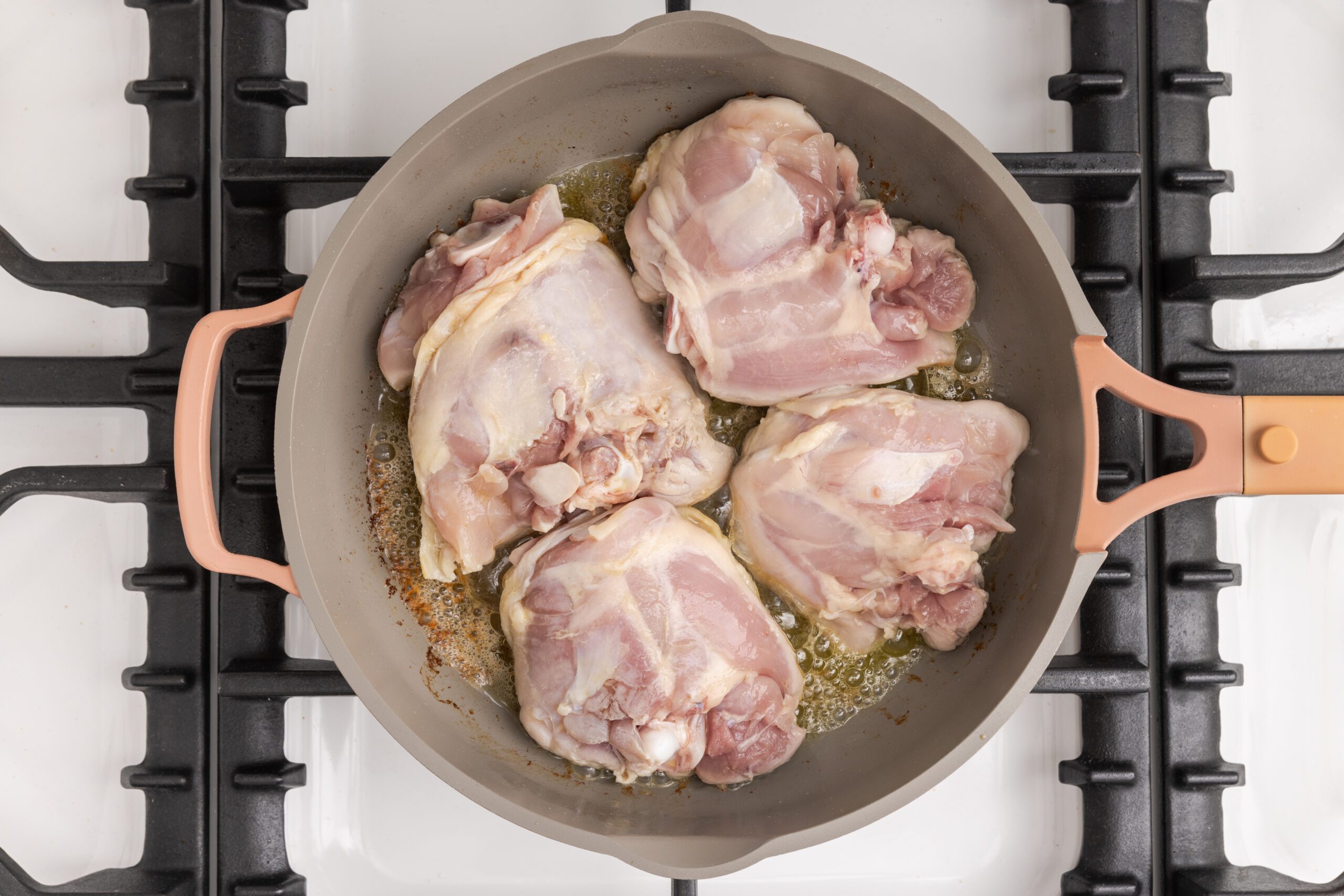 Chicken thighs being browned in large skillet.