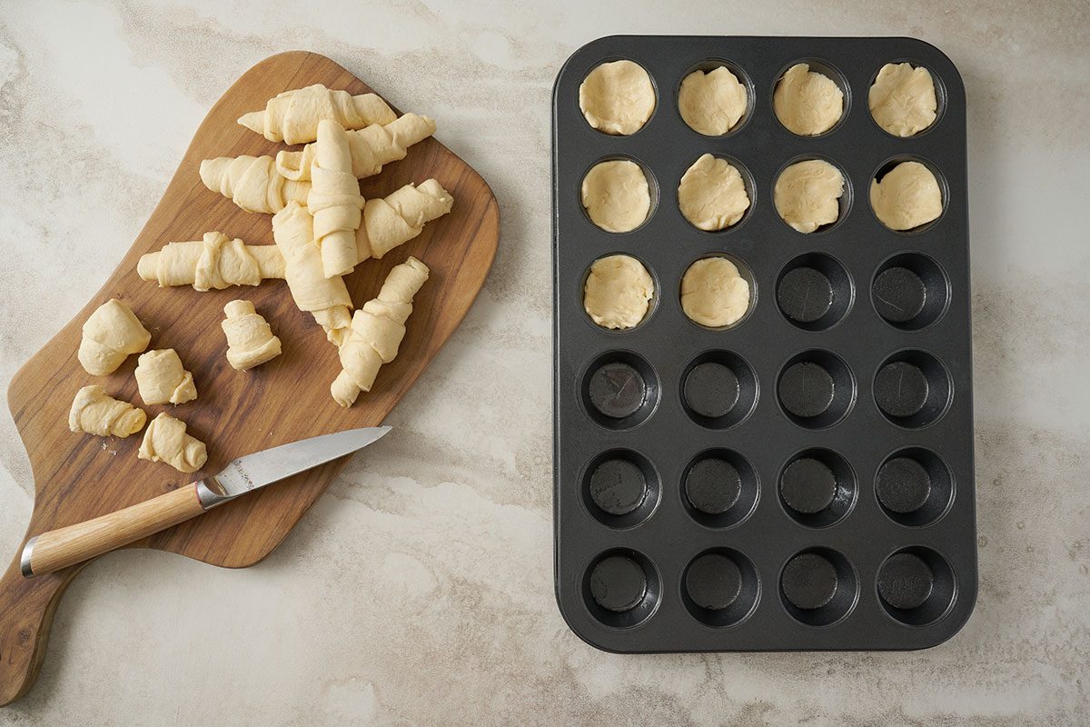 Overhead view of crescent roll dough being pressed into miniature muffin cups, forming a well for the toppings in the Taste of Home Pizza Bites recipe.