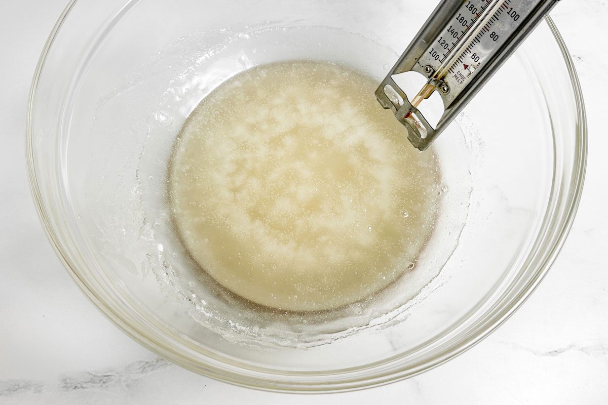 Sugar syrup for Taste of Home Pecan Brittle in a glass bowl with candy thermometer