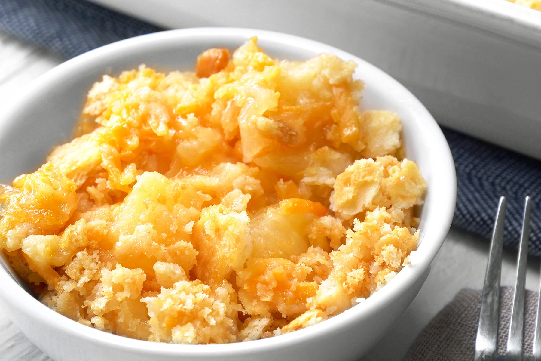 A close-up view of a bowl filled with Pineapple Casserole, The topping is a buttery, crumbly mixture, likely made from crushed crackers or cookies;