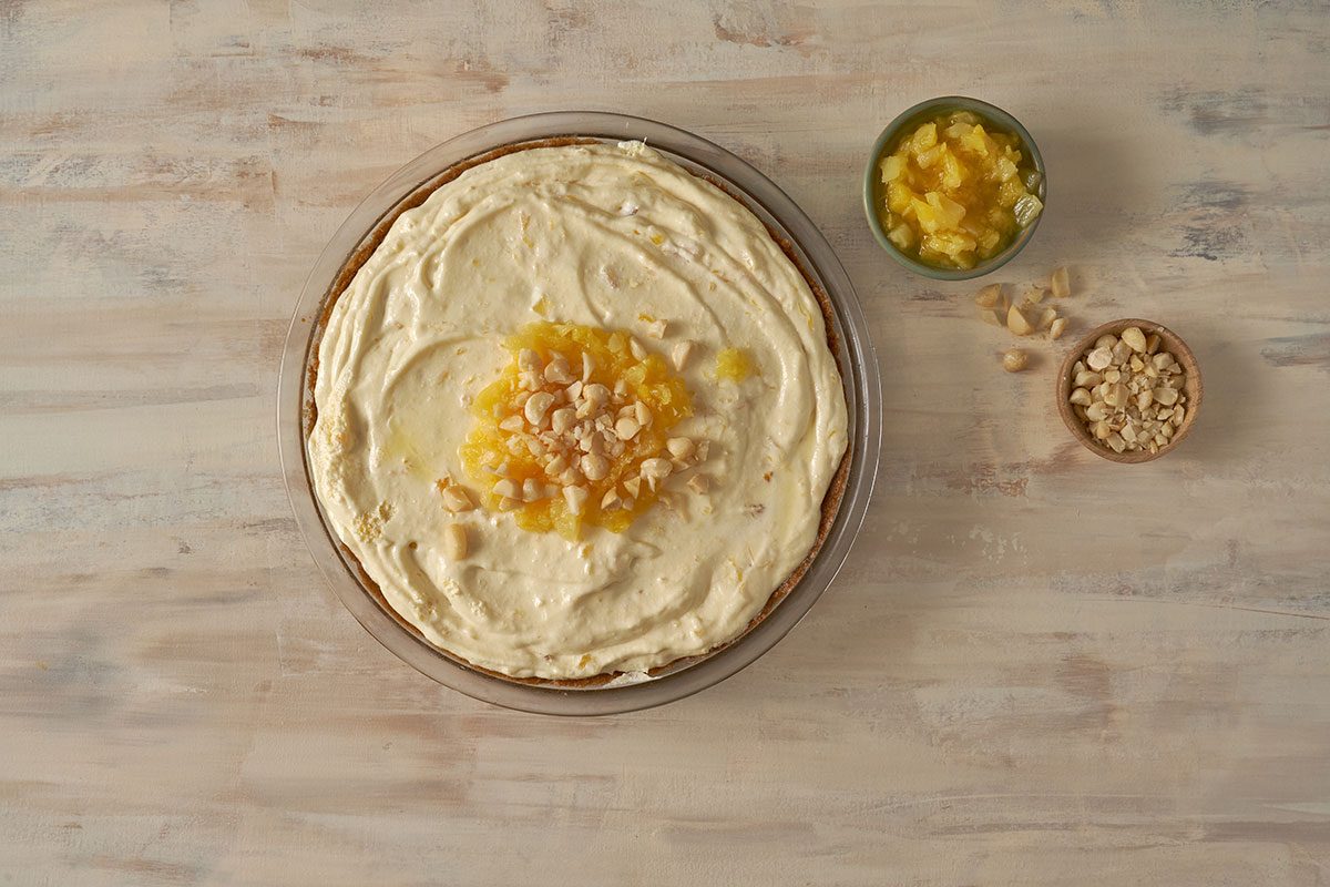 An overhead view of the Pineapple Pie in a graham cracker crust, topped with toasted macadamia nuts and crushed pineapple, by Taste of Home.