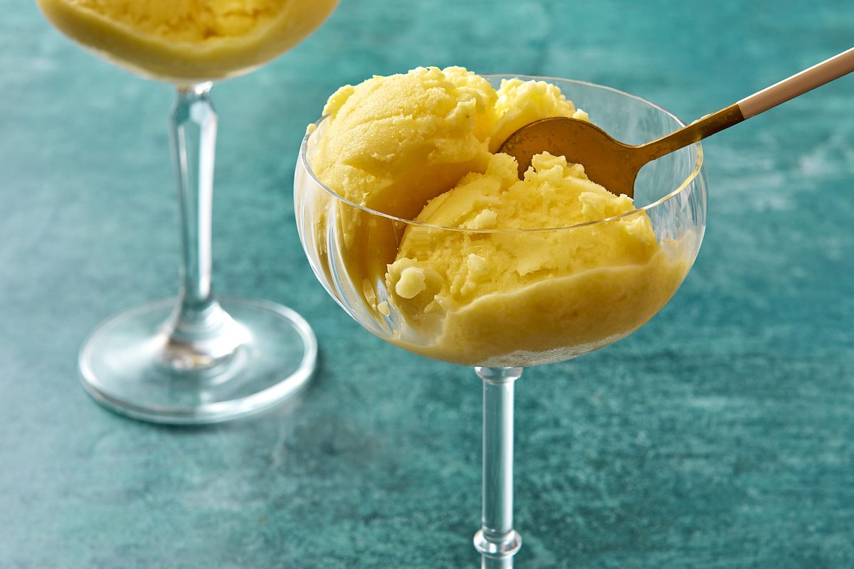 Closeup of scoops of pineapple sherbet being served out of a cocktail glass with a spoon