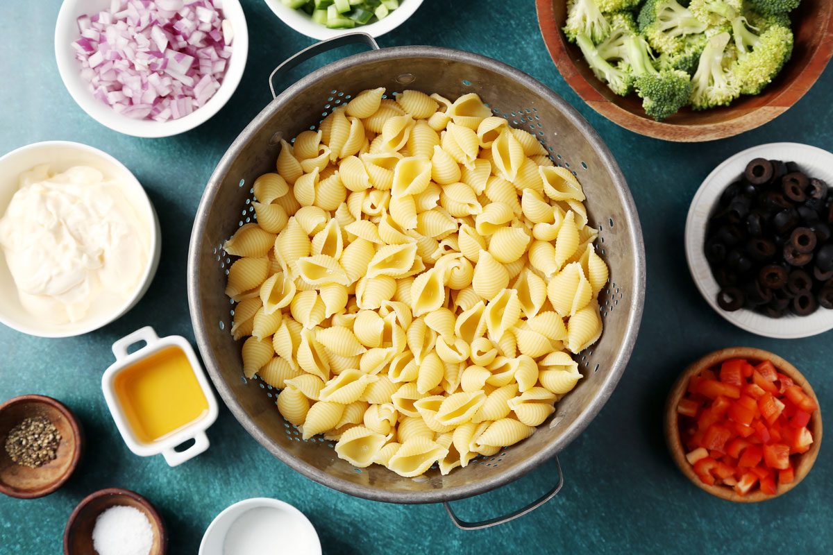 Process of making Taste of Home's Creamy Pasta Salad in a large mixing bowl on a green surface.