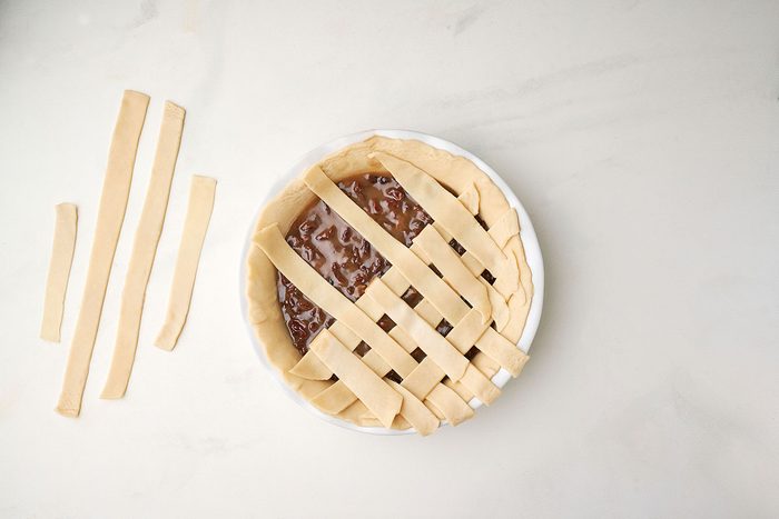 Creating a lattice pie crust for Taste of Home's Raisin Pie recipe, trimming the edges to seal the filling.