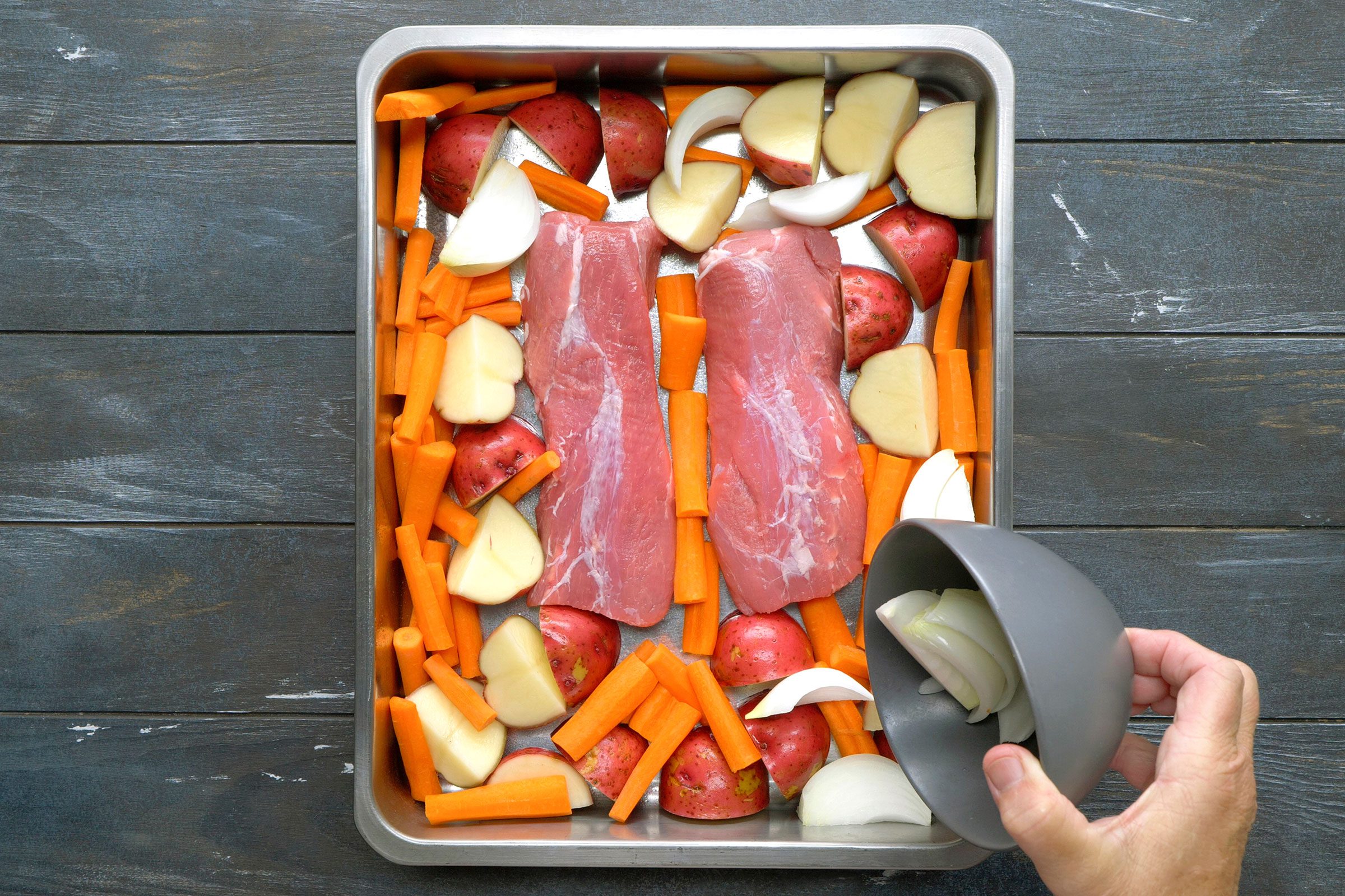 Arranging potatoes, carrots and onion around the pork
