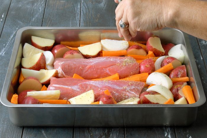 Adding seasoning to the pan containing pork, fruits and vegetables