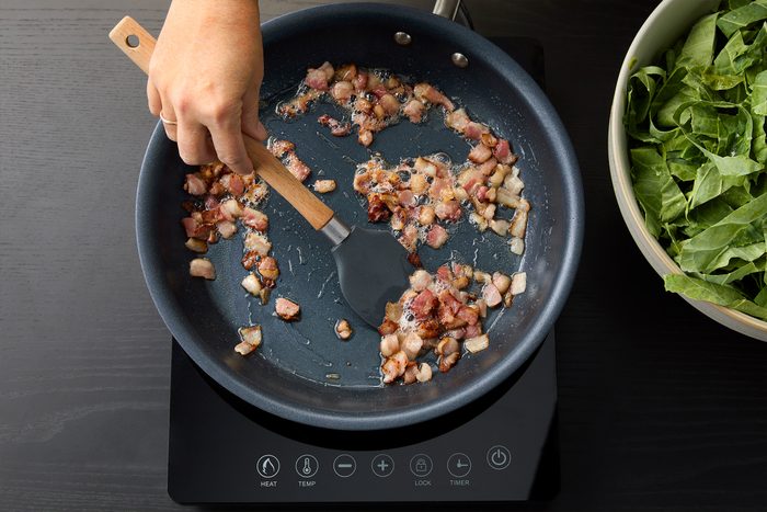 Cooking bacon pieces in a large skillet to prepare Sauteed Collard Greens