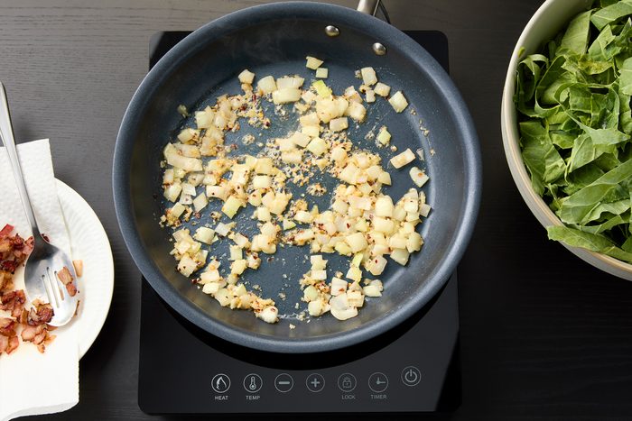 Cooking onion garlic and red chilli flakes and cooked bacon on the side on a paper towel