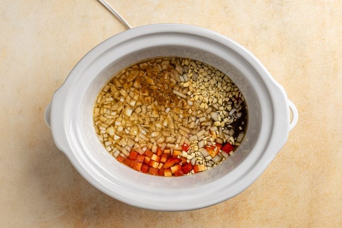 combining all of the ingredients, except the corn and parsely, in the slow cooker.