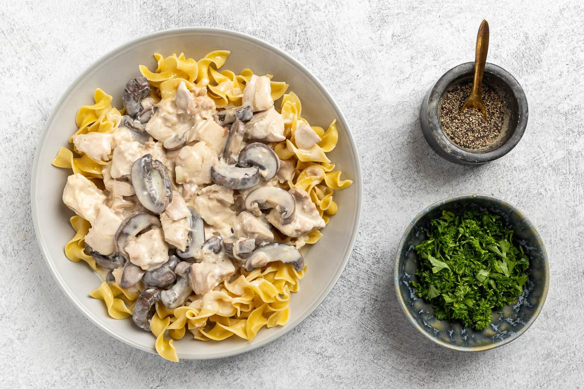 plating Slow Cooker Chicken Stroganoff with fresh parsley and black pepper for garnish.