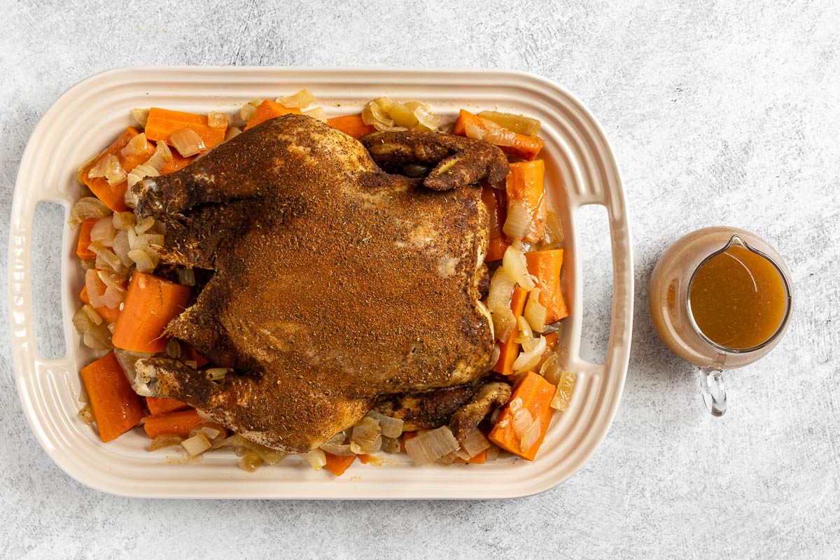 chicken and vegetables on a serving platter with the cooking juices on the side.