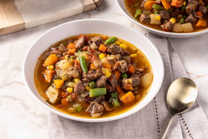 Slow Cooker Vegetable Soup in a white bowl next to cutting board and spoon