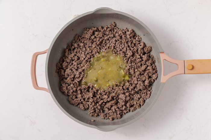 Beef cooked in skillet being combined with sauce mixture.