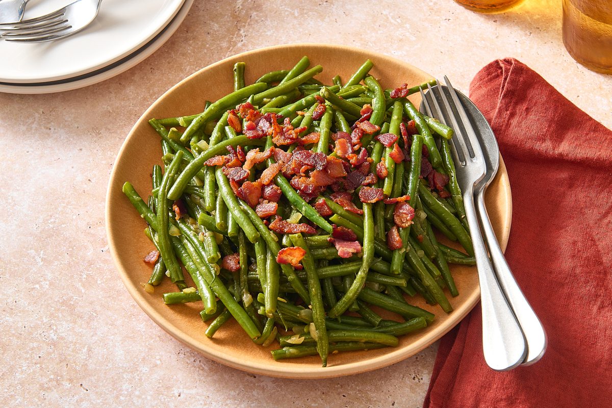 Angled shot of a plate of Southern green beans topped with crispy bacon