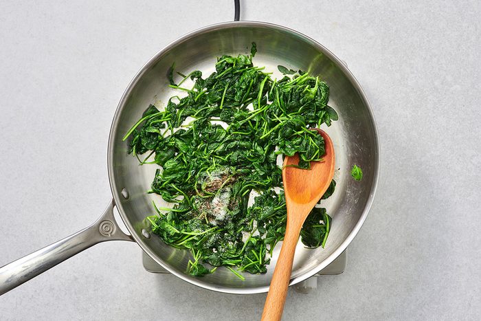 Wilted spinach in a skillet with vinegar sugar and pepper stirred in