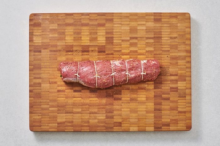 Rolled pork tenderloin tied with kitchen string on a cutting board