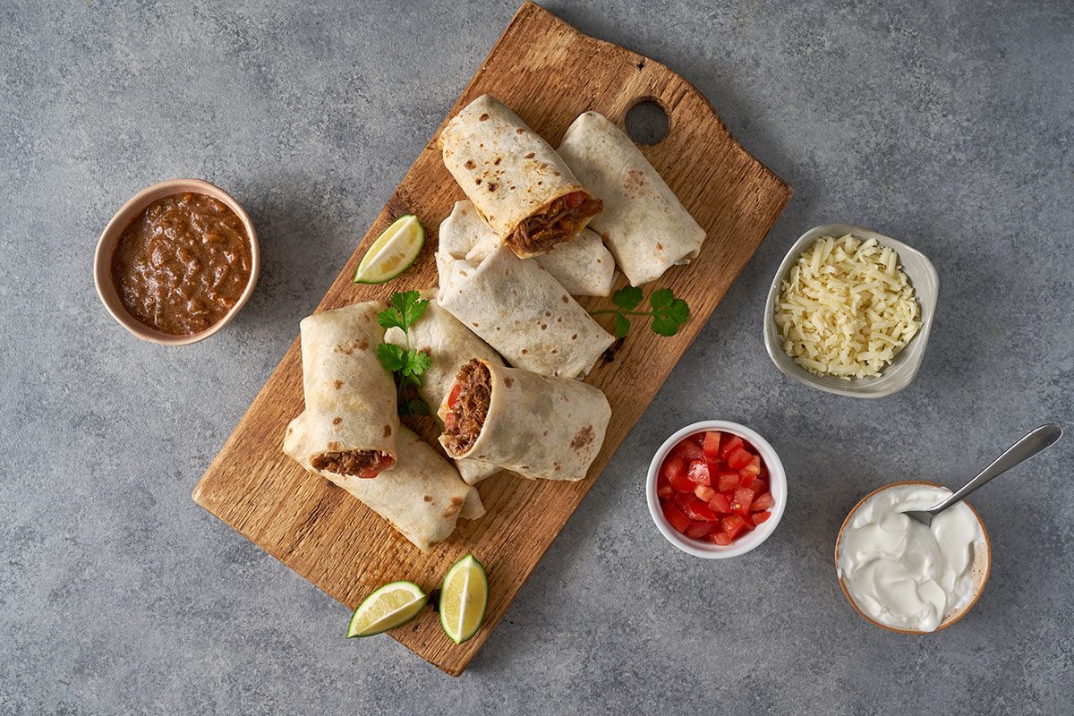 A delicious platter of assembled Shredded Steak Burritos, garnished with fresh toppings like cheese, tomatoes, and sour cream.