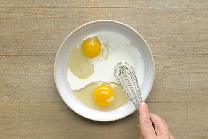 overhead shot of eggs and milk being whisked in a shallow bowl on a wooden surface