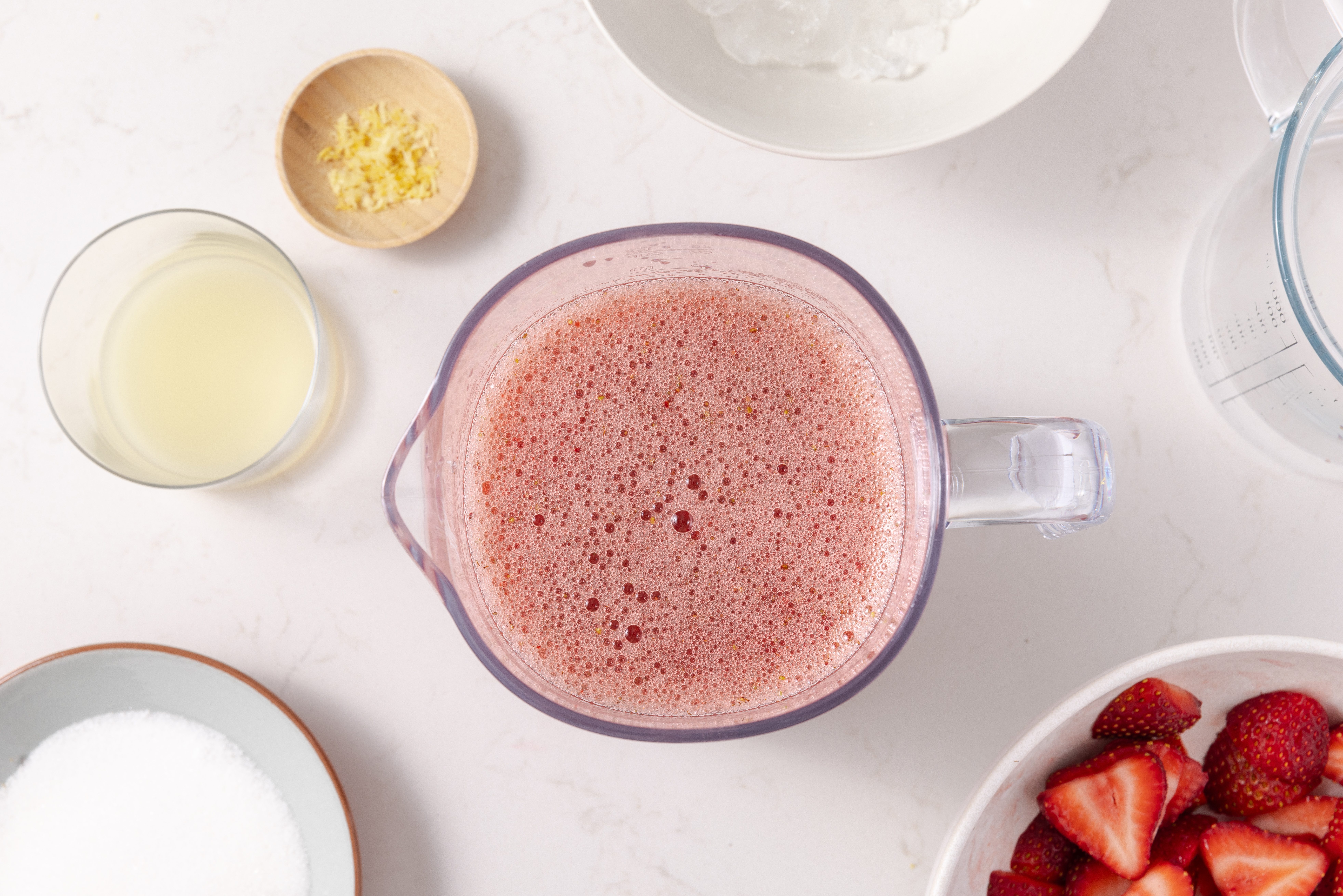 Strawberry drink being prepared in blender with strawberries, lemon juice, lemon zest, sugar and ice.