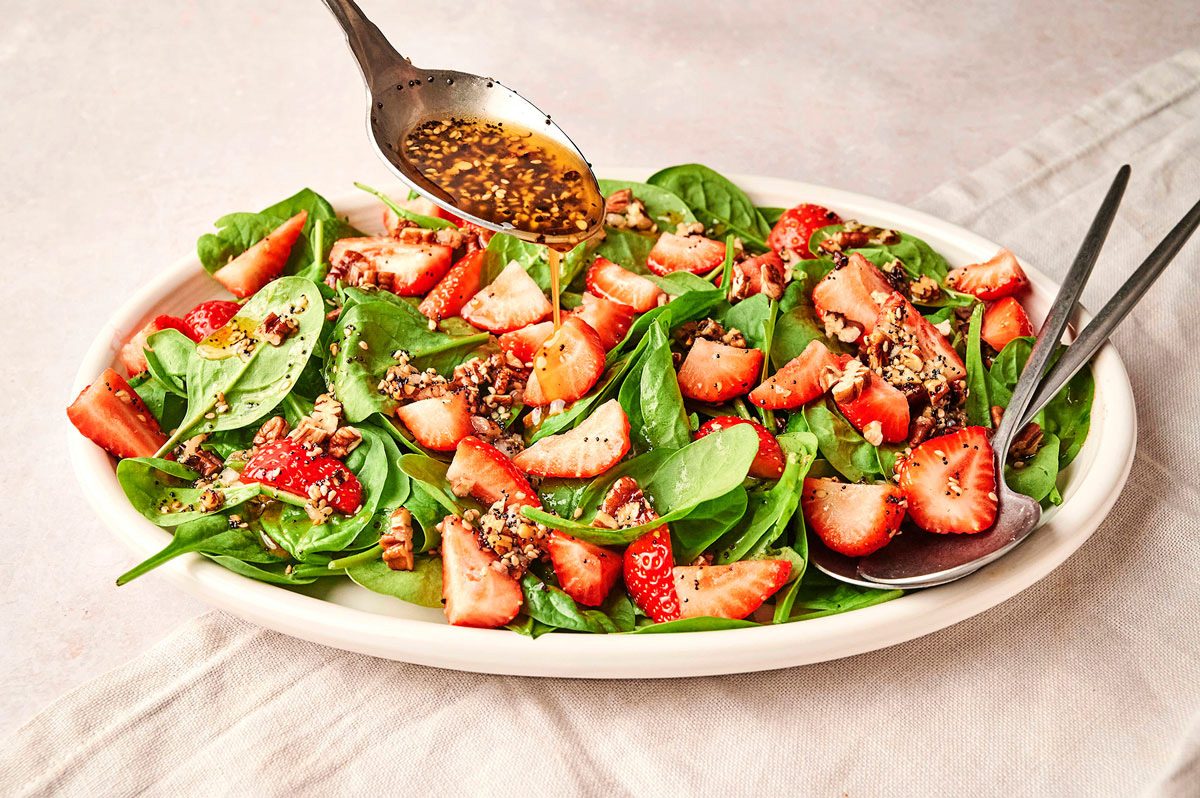 Dressing being drizzled with a metal spoon over the Strawberry Spinach Salad recipe by Taste of Home