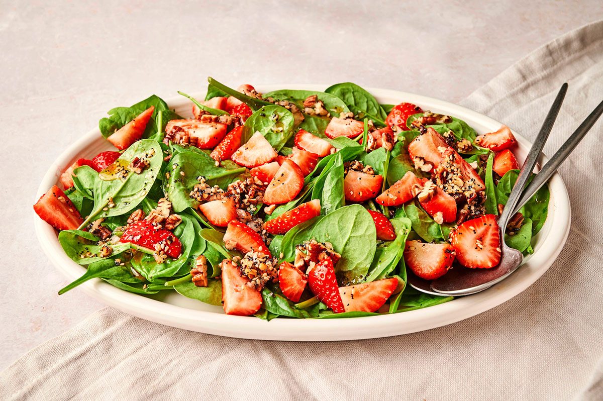 A large white platter showing the strawberry spinach salad recipe by Taste of Home, with metal serving spoons
