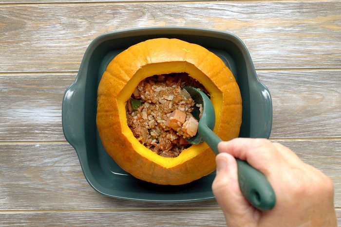 overhead shot of the pumpkin in a shallow baking dish with a hand adding the filling into the top