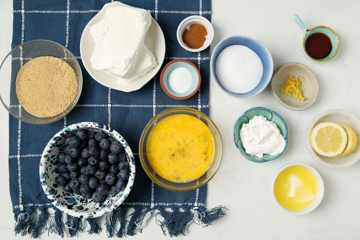 Ingredients for Taste of Home's Blueberry Cheesecake Bars laid out in small bowls on a white wooden surface.