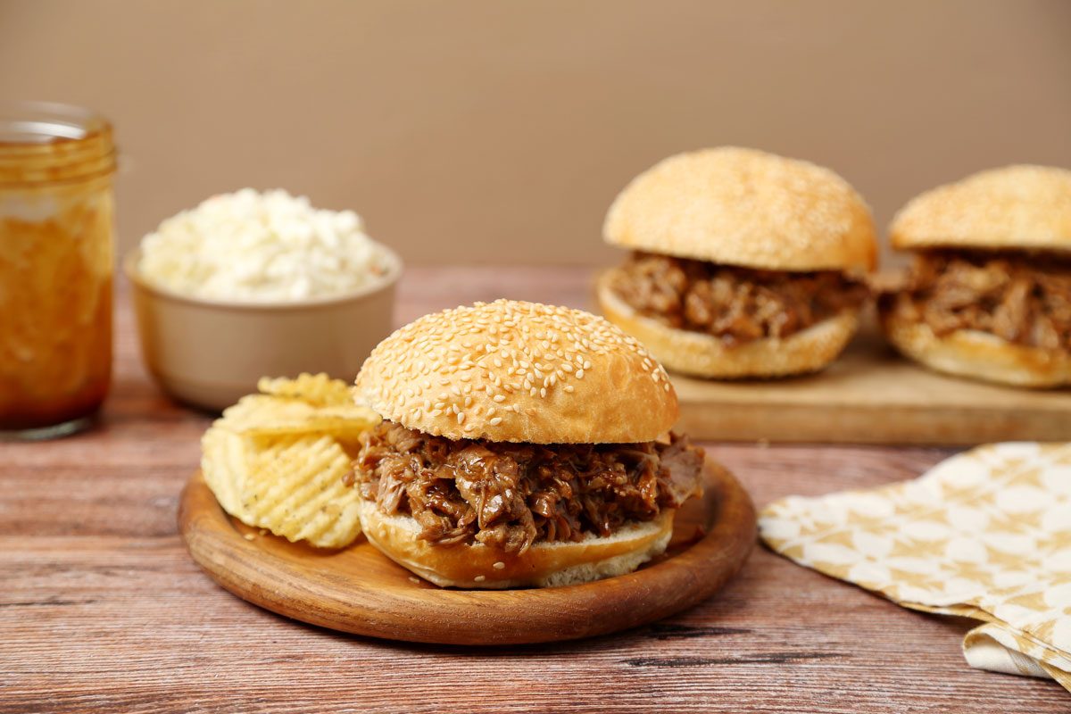 Close up of Taste of Home's Root Beer Pulled Pork assembled and on a wooden board on a dark brown wooden surface.