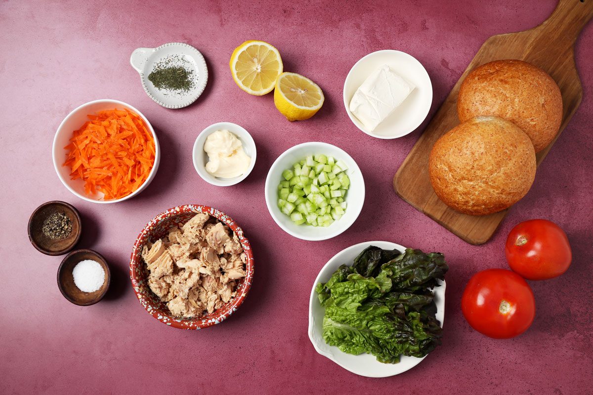 Ingredients for Taste of Home's salmon salad sandwich laid out in small bowls on a magenta surface.