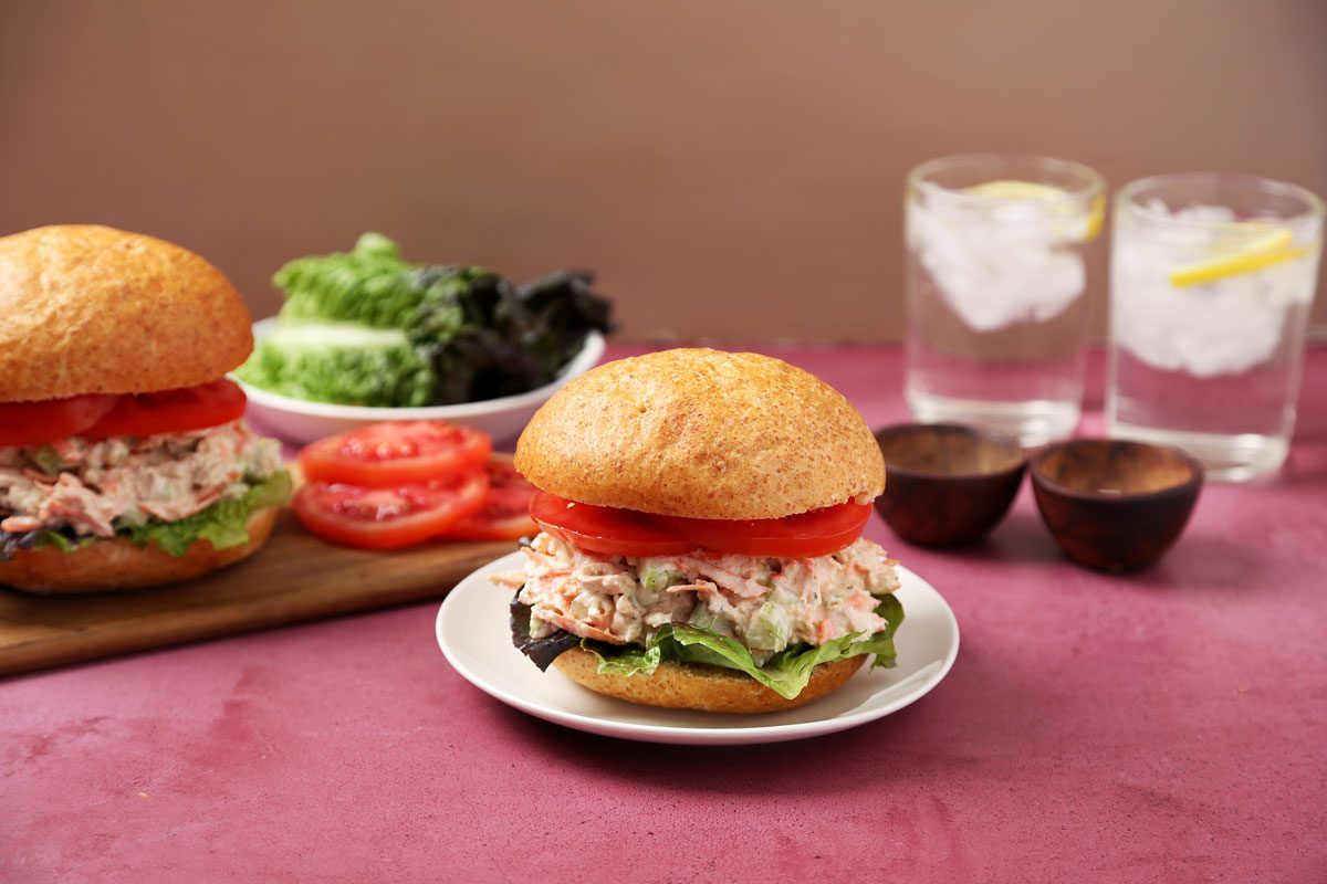 Close up of Taste of Home's salmon salad sandwich on a wooden board and a magenta surface.