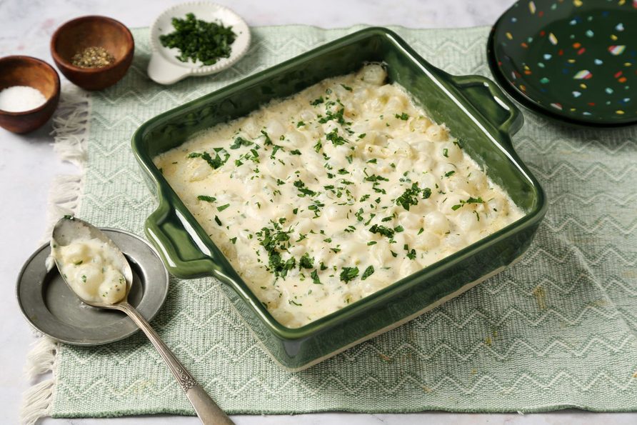 Close up of Taste of Home's Creamed Pearl Onions in a green casserole dish on a grey marble surface.