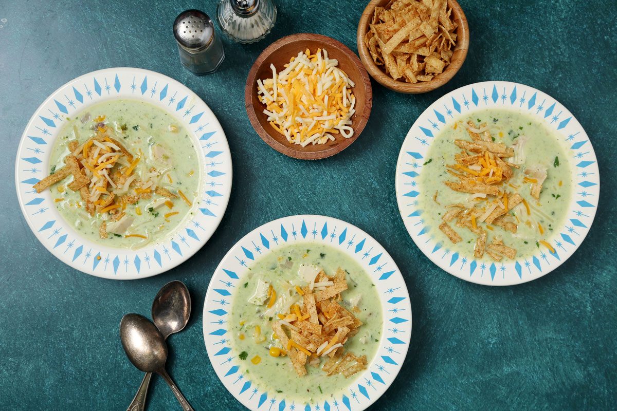 Close up of Taste of Home's Poblano Soup served in blue and white bowls on a teal surface.
