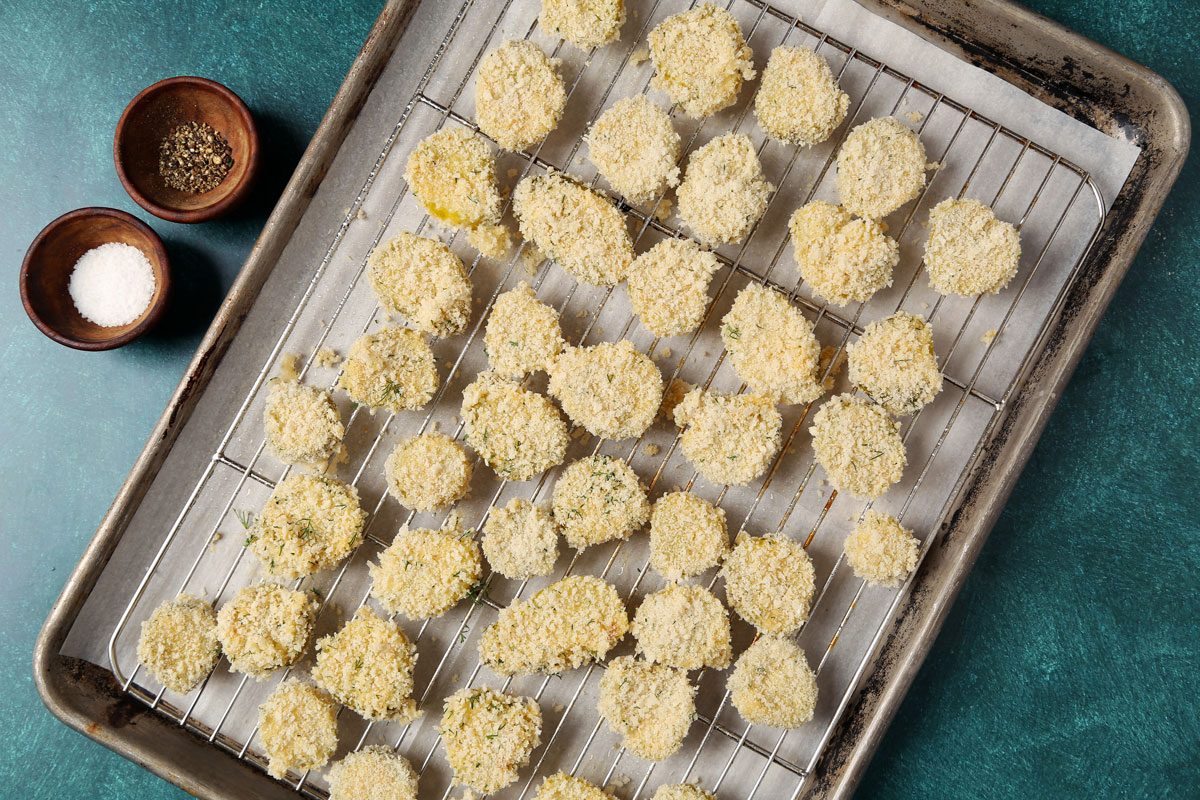 Process of making Taste of Home's Oven Fried Pickles on a wire rack and baking sheet on a teal surface.