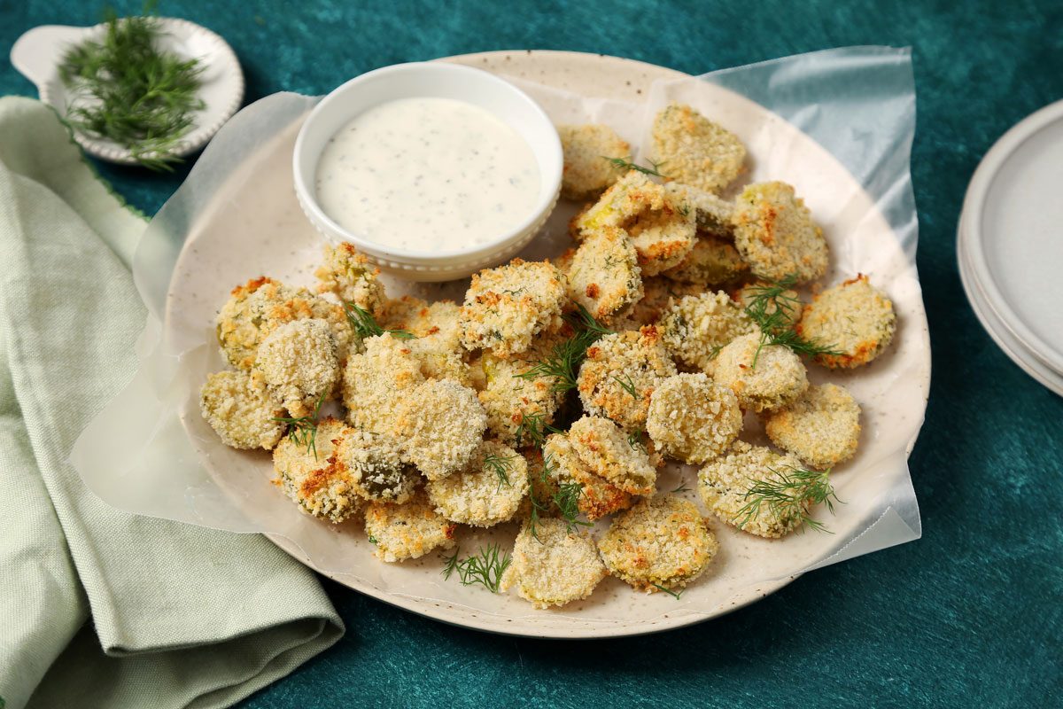 Close up of Taste of Home's Oven Fried Pickles on a plate with ranch on a teal surface.