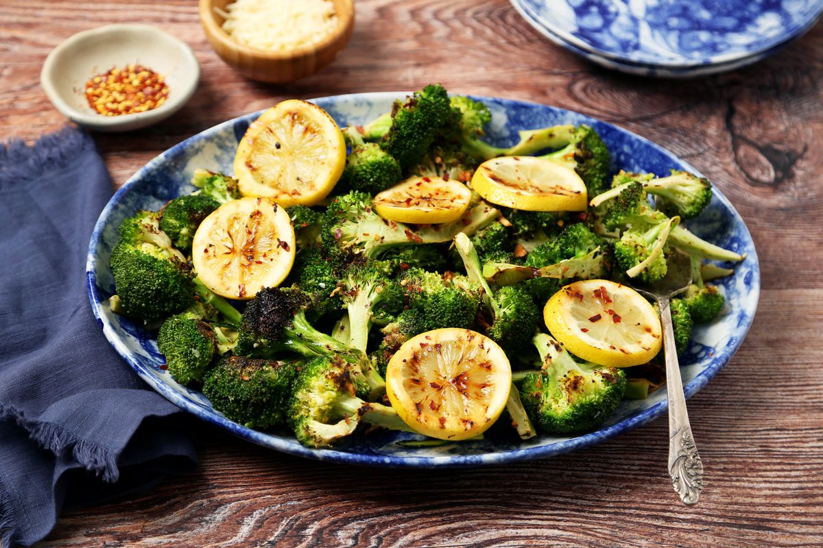 Close up of Taste of Home's Grilled Broccoli served on blue plates and a platter on a brown wooden surface.