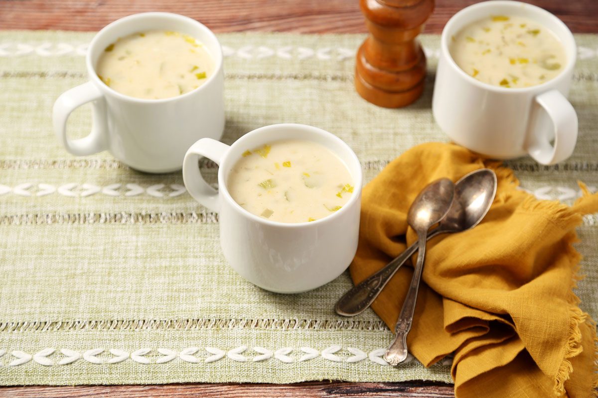 Close up of Taste of Home's Cream of Celery Soup served in white mugs on a brown wooden surface.