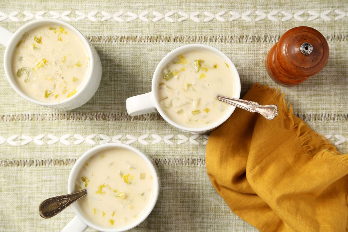 Close up of Taste of Home's Cream of Celery Soup served in white mugs on a brown wooden surface.