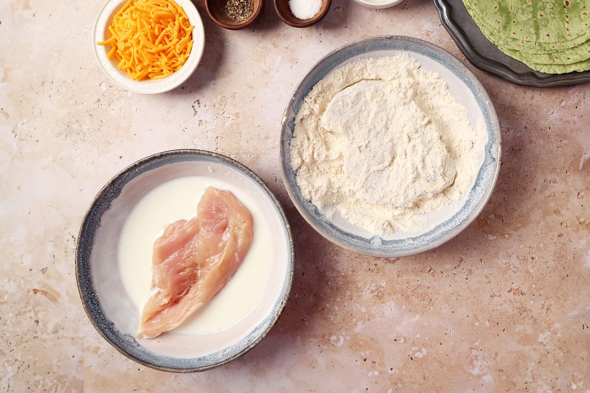Process of making Taste of Home's Buffalo Chicken Wrap. Chicken being dredged in a bowl of flour and buttermilk.