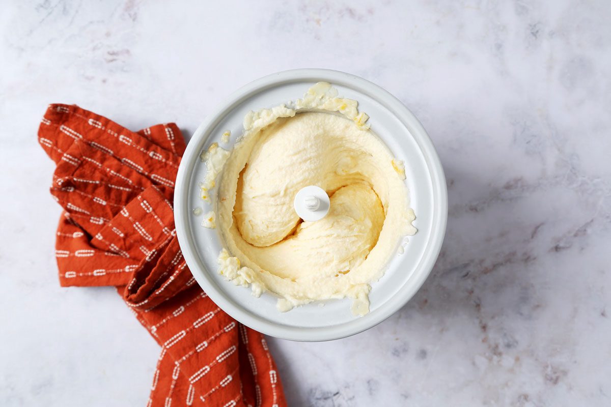 Process of making Taste of Home's Orange Sherbet in an ice cream maker on a white marble surface with an orange towel.