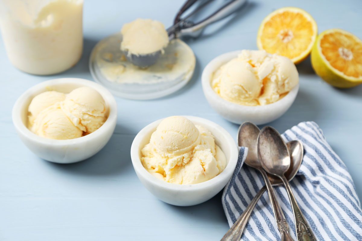 Close up of Taste of Home's Orange Sherbet served in white bowls on a white marble surface with an orange towel.