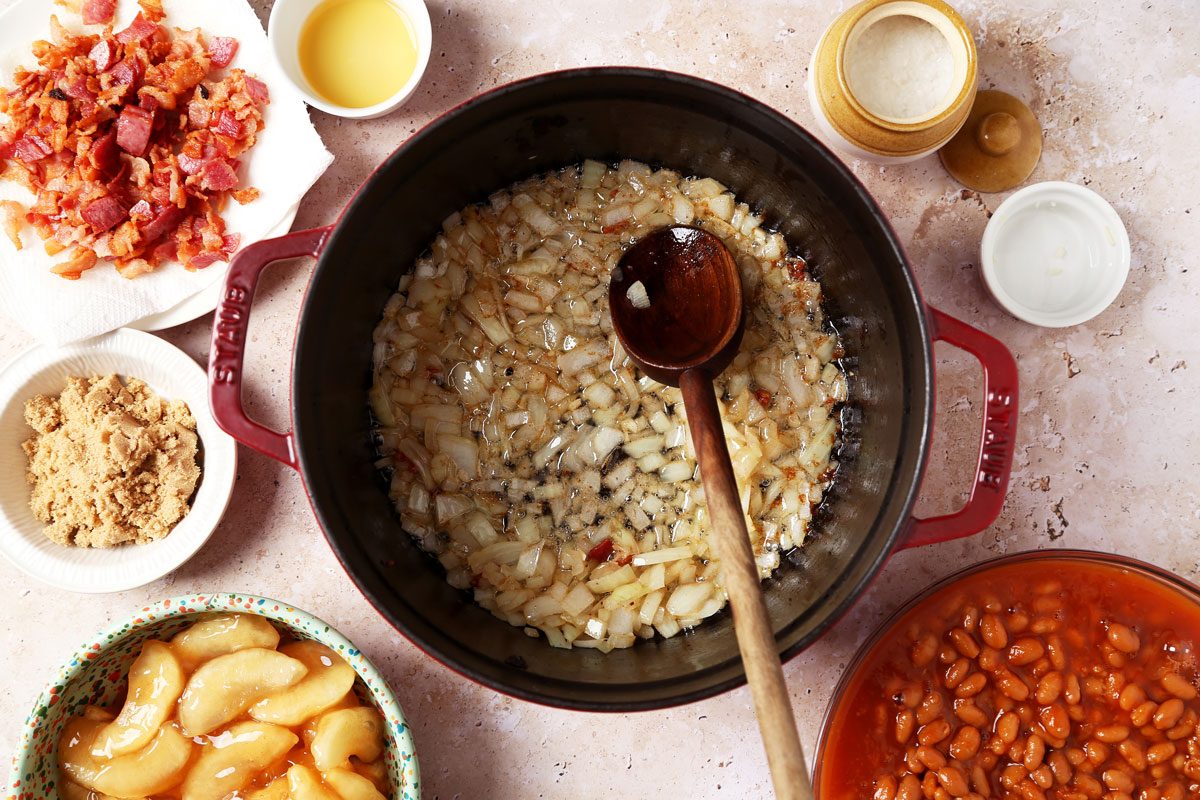 Process of making Taste of Home's Apple Pie Baked Beans in a large pot on a brown marble surface.