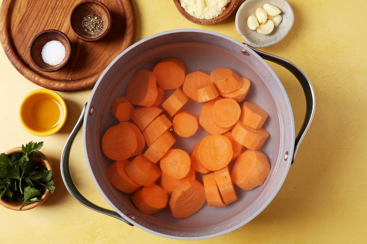 Process of making Taste of Home's Smashed Sweet Potatoes on a large baking sheet on a yellow surface.