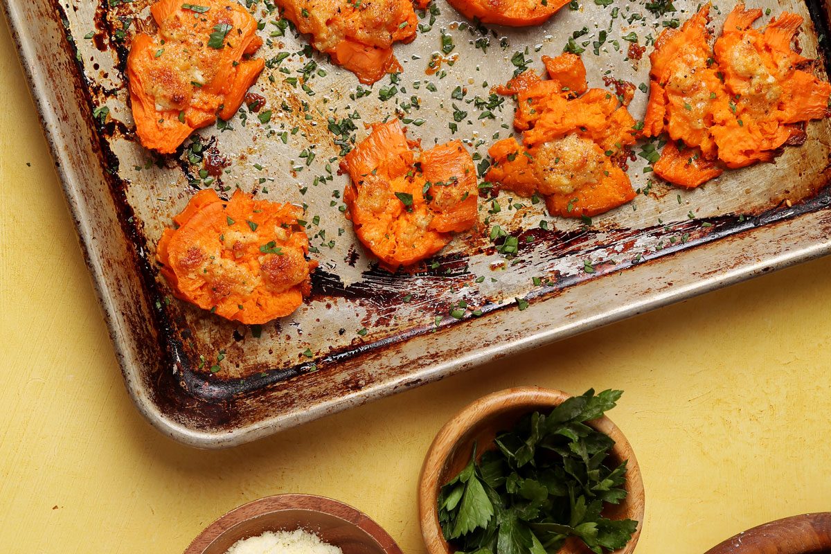 Close up of Taste of Home's Smashed Sweet Potatoes on a large baking sheet on a yellow surface.
