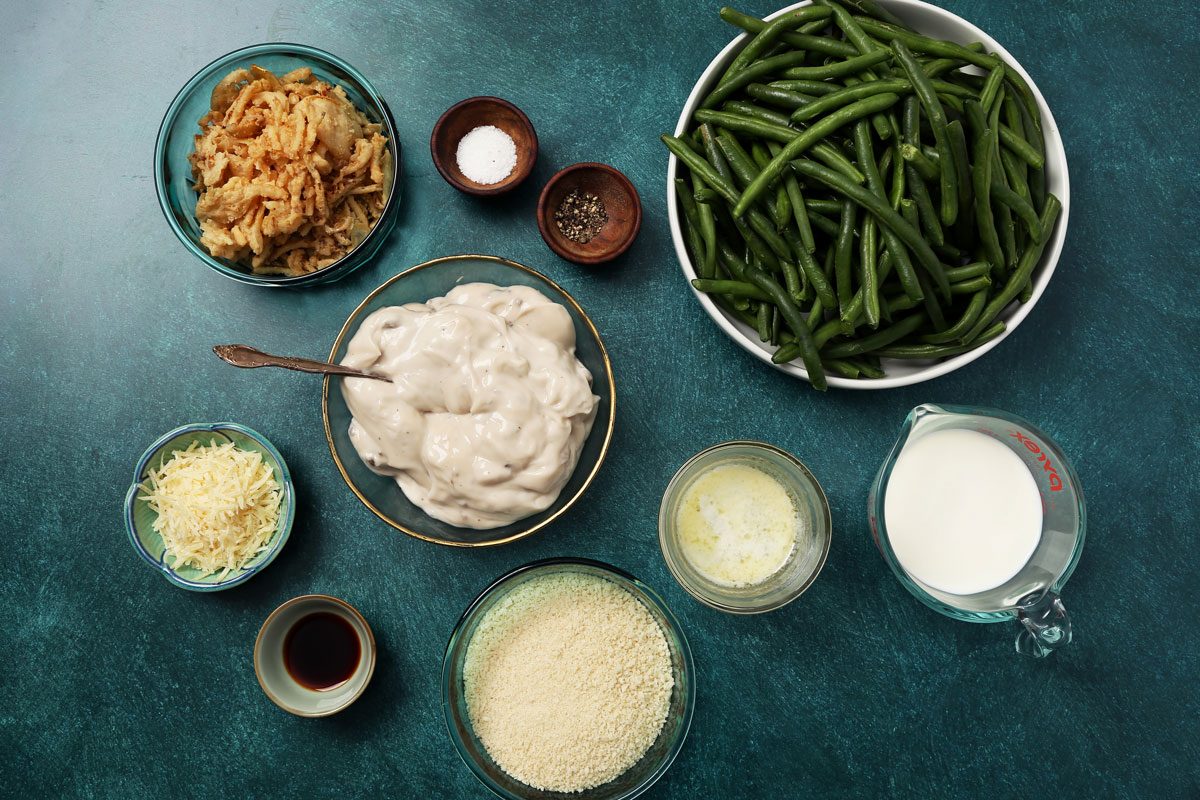 Ingredients for Taste of Home's Gluten Free Green Bean Casserole laid out in small bowls on a teal surface.