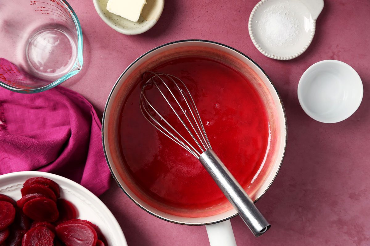 Process of making Taste of Home's Harvard Beets making sauce in a saucepan on a magenta surface.