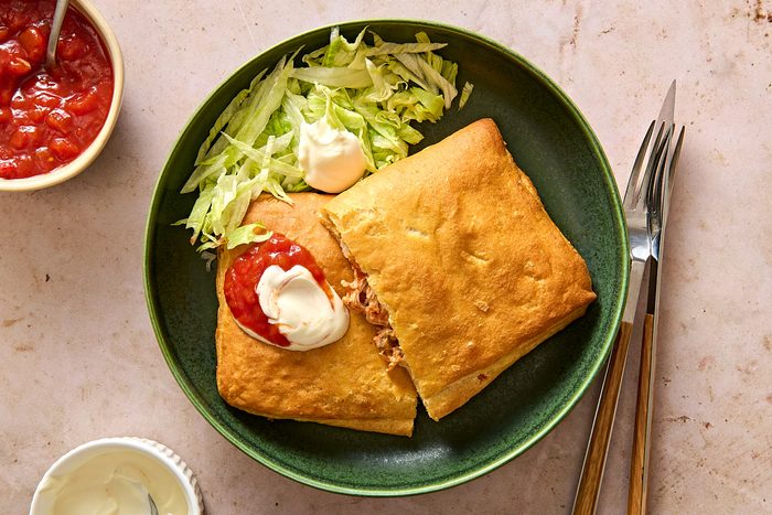 Overhead shot of a taco pocket cut in half on a plate with lettuce, sour cream and salsa
