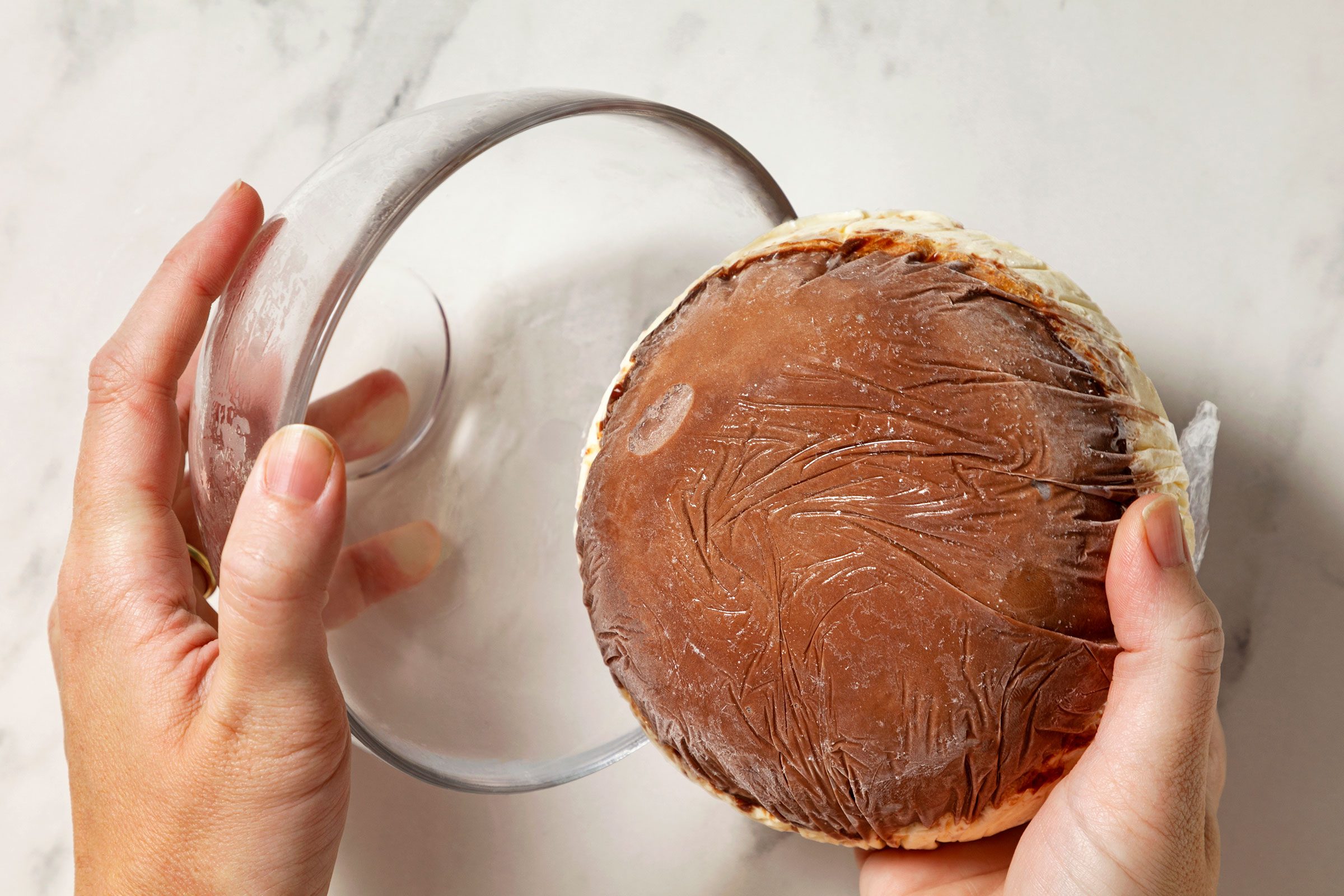 Removing frozen chocolate ice cream from storage wrapped bowl