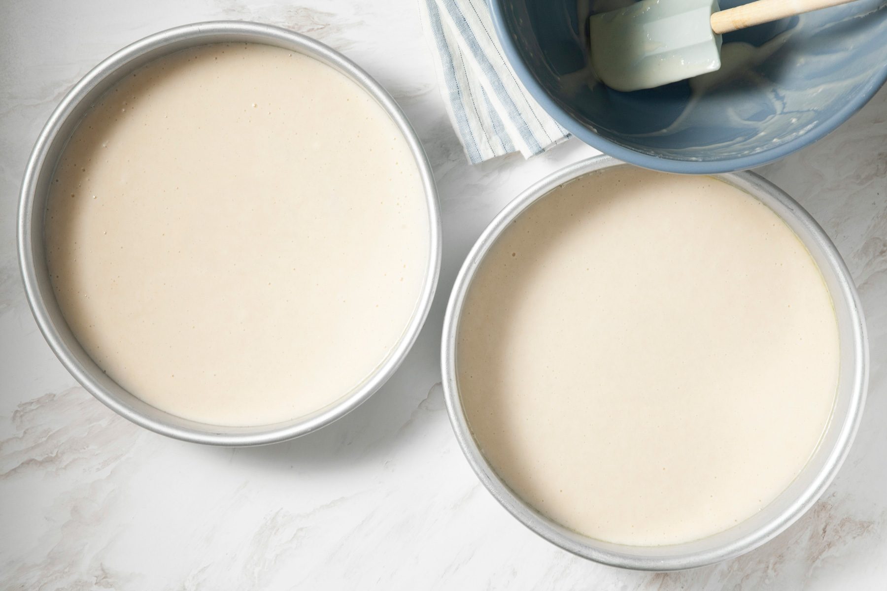 Vegan birthday cake batter poured into two greased round baking pans.