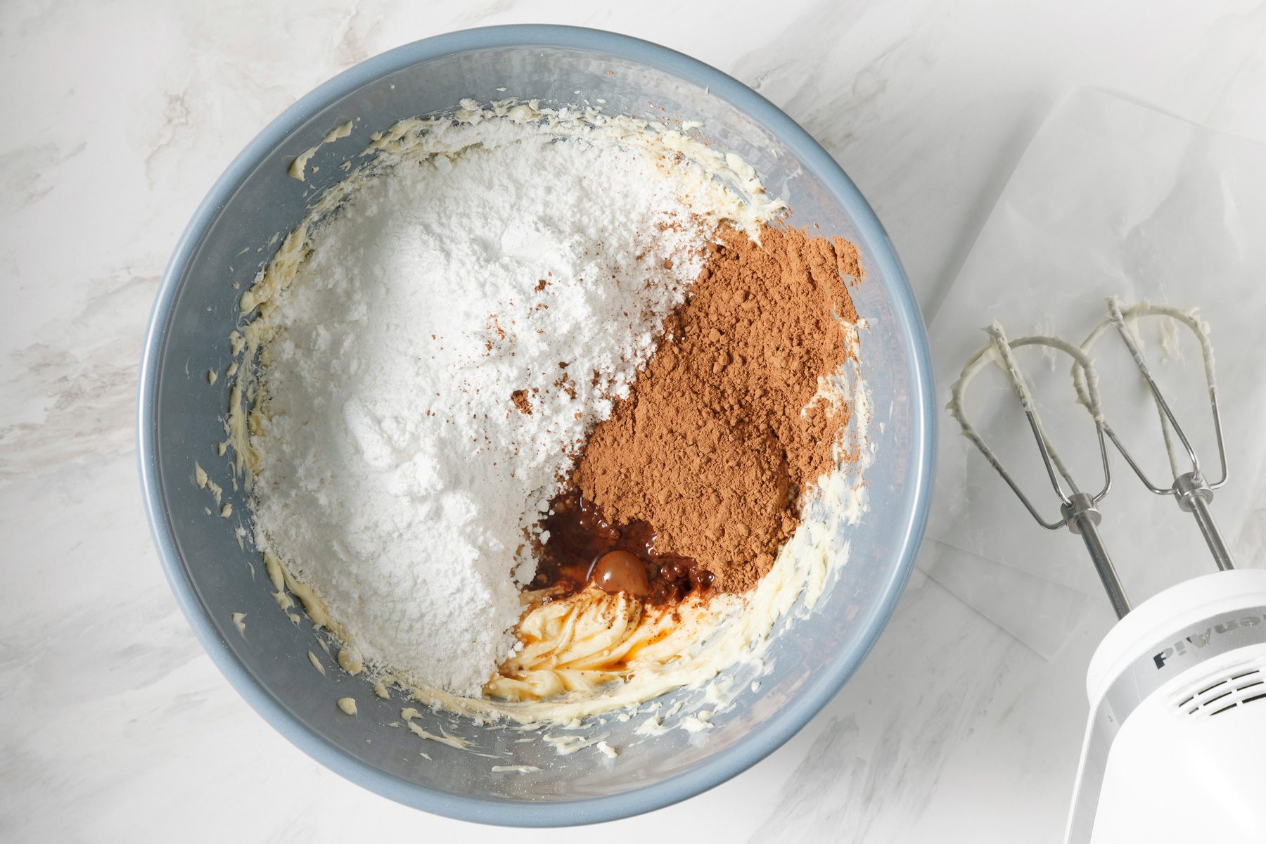 Confectioners' sugar, baking cocoa, and vanilla extract are added to the bowl.