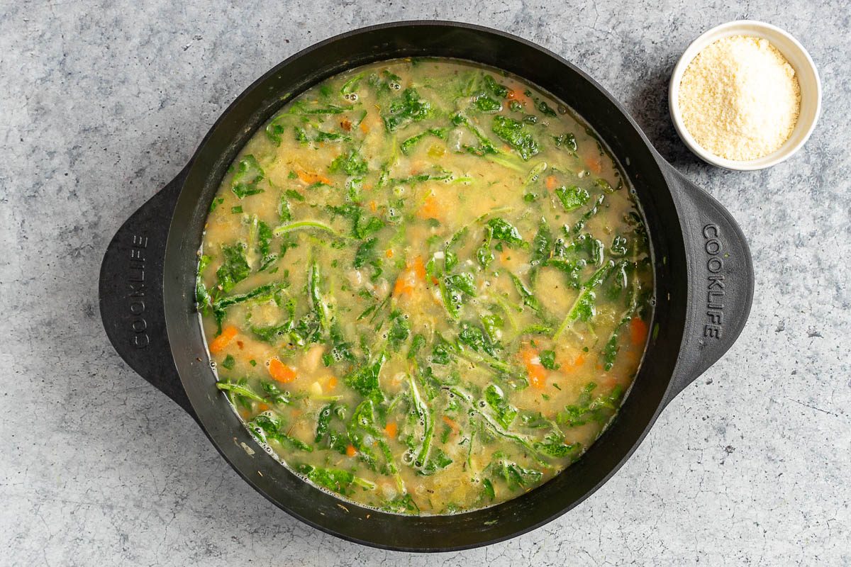 Taste of Home White Bean and Kale soup photo of the kale and parsley added to the soup with grated Parmesan.